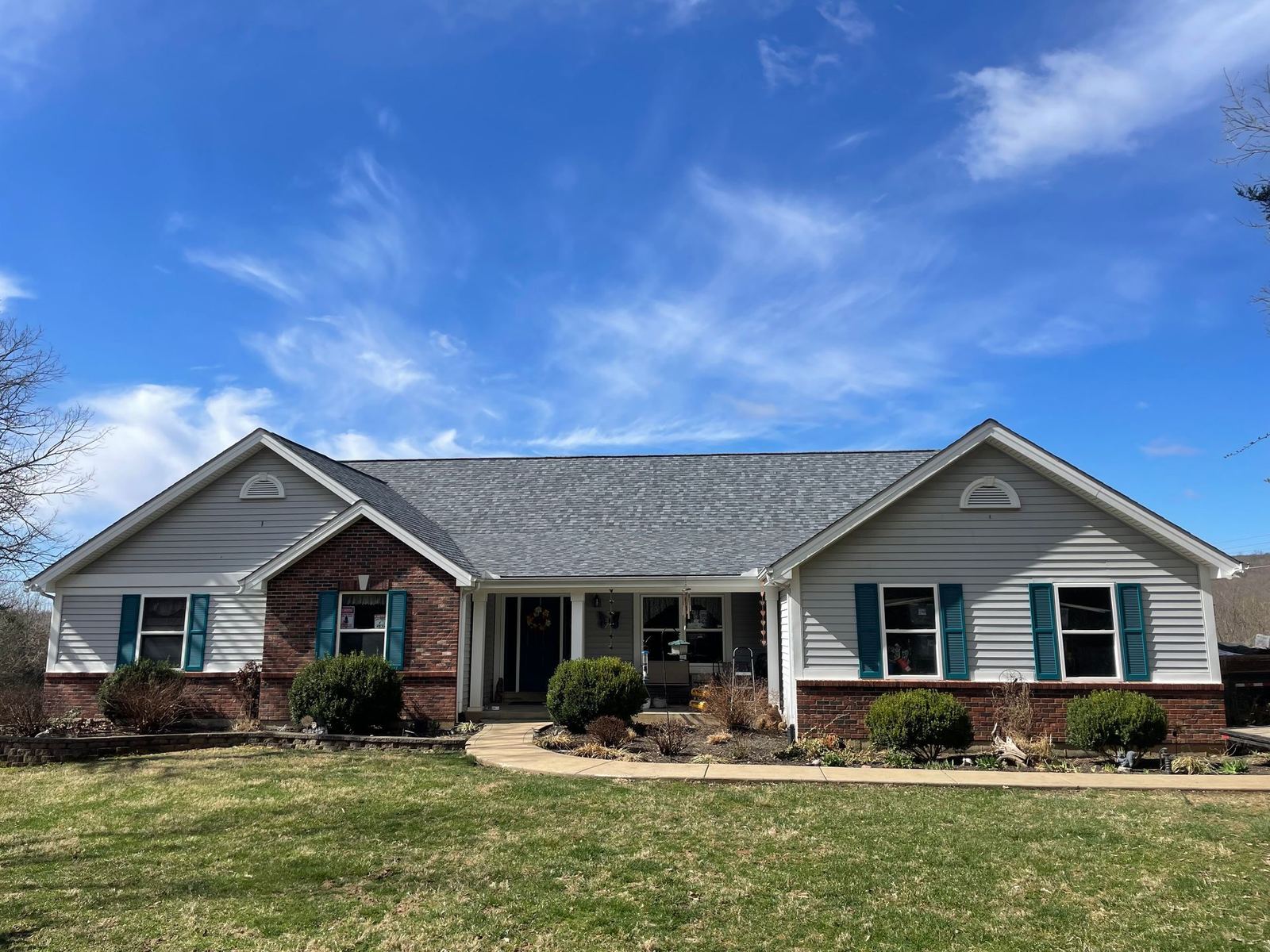 Ranch-style house with gray siding, brick accents, blue shutters, and a gray roof under a blue sky.