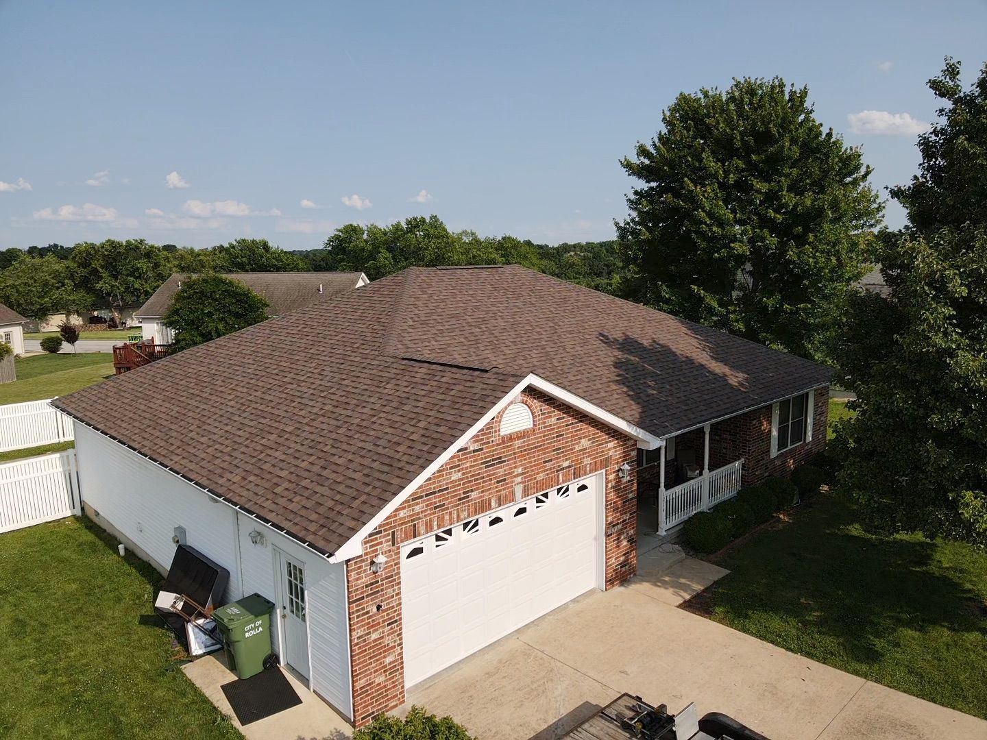 House with brown roof, brick accents, and white garage door under a blue sky.