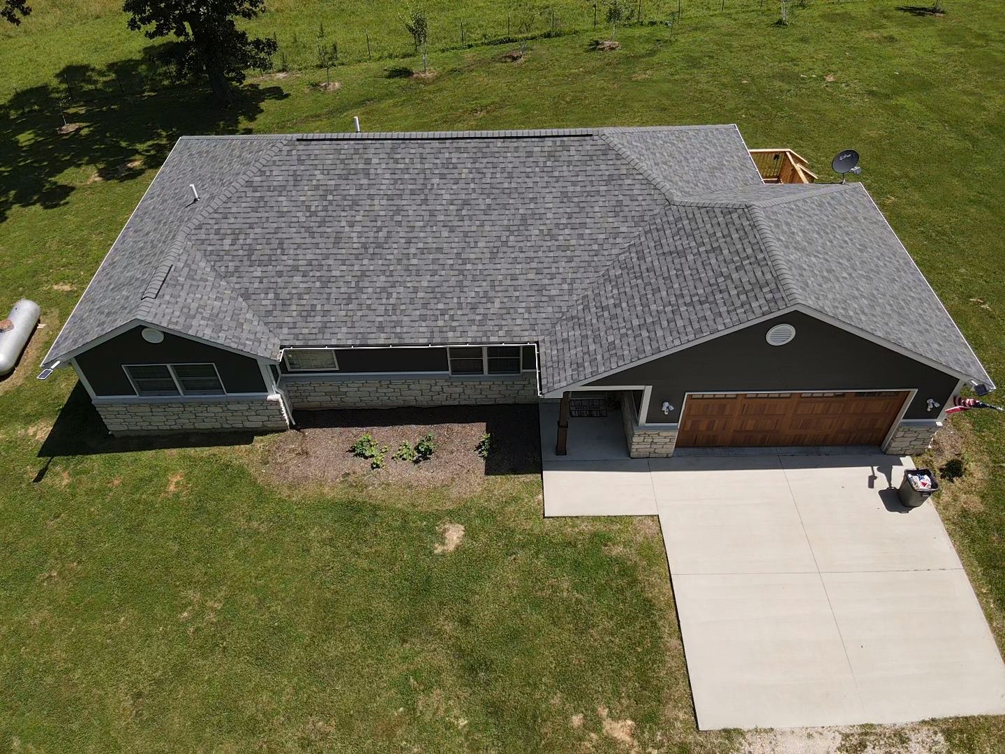 Overhead view of a house with a gray roof, brown garage door, and concrete driveway on a grassy lot.
