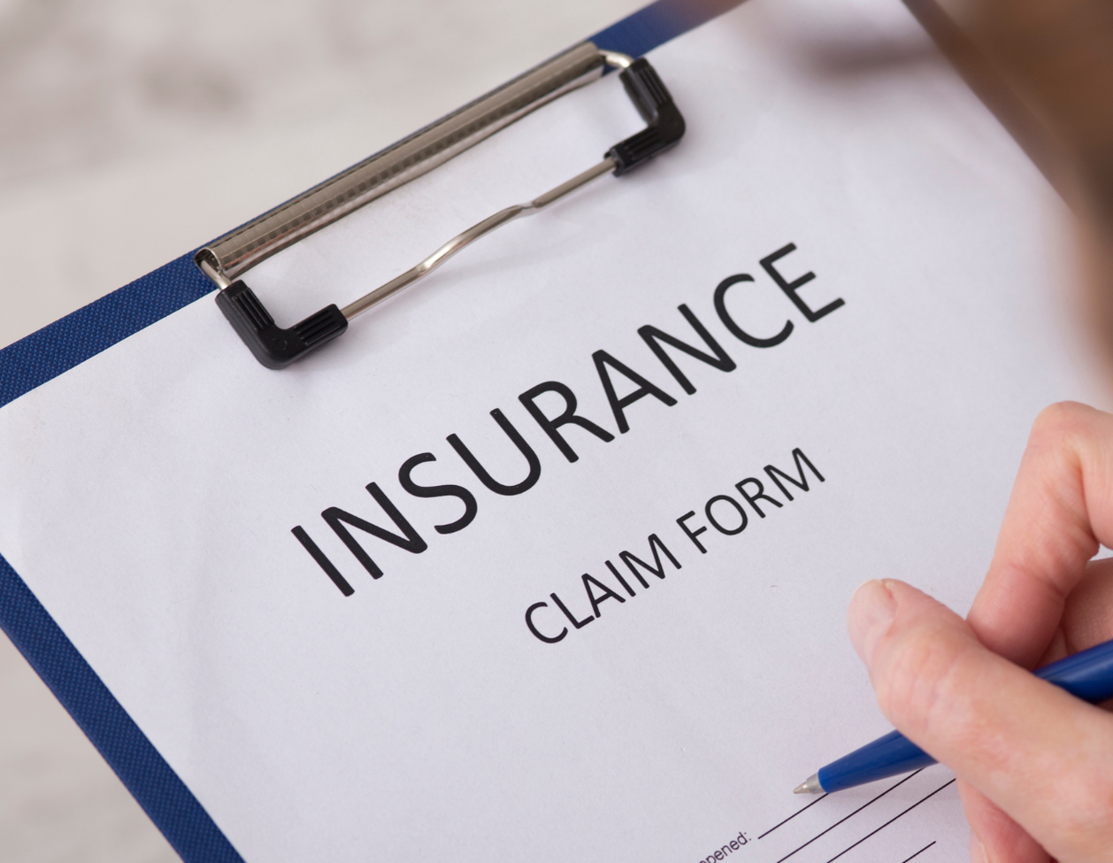 Person filling out an insurance claim form on a clipboard with a pen.