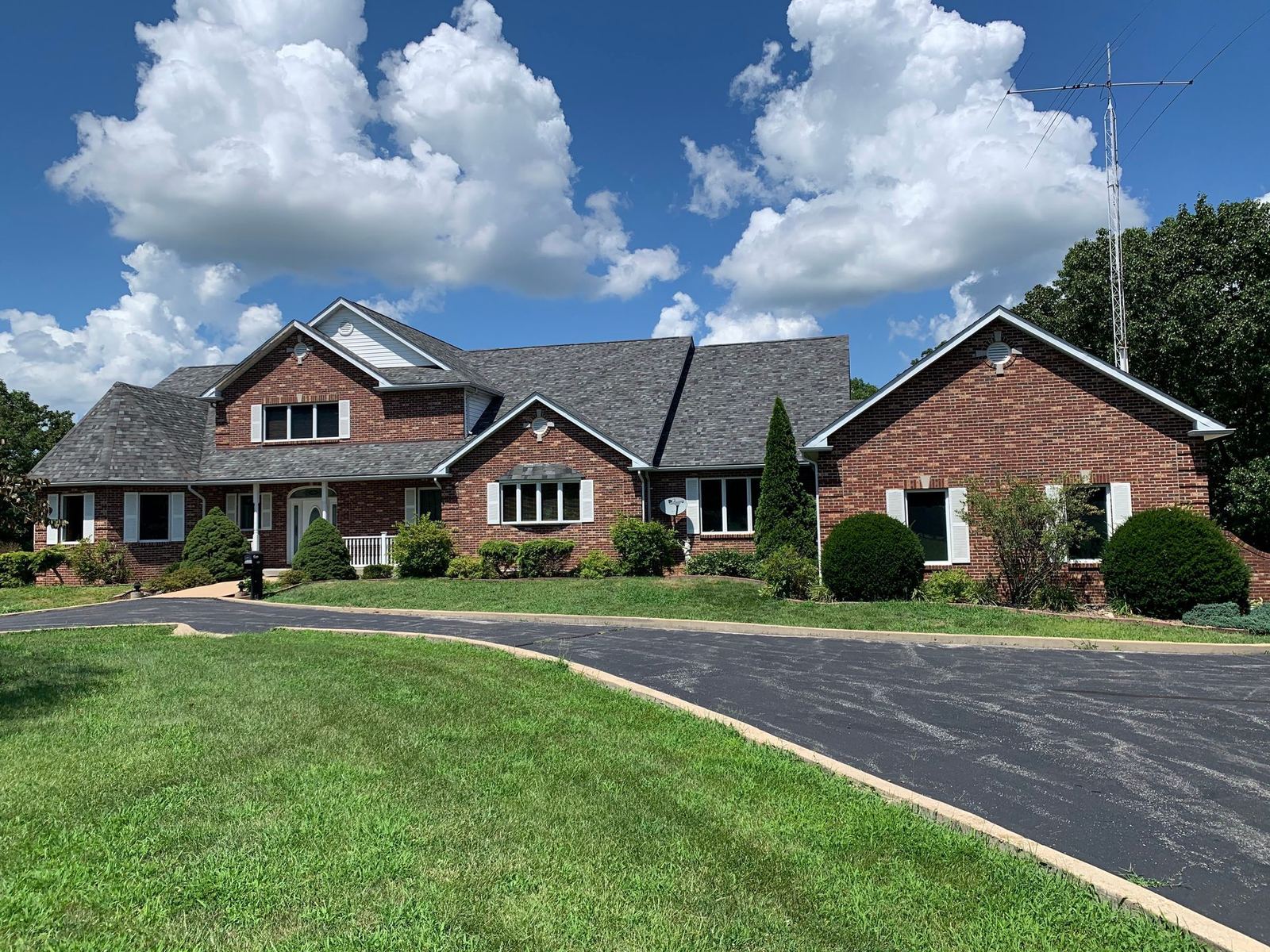 Brick house with asphalt driveway on a sunny day. Green lawn, white trim, and fluffy clouds.