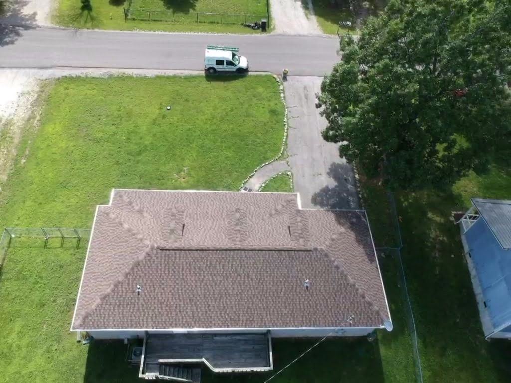 Overhead view of a house with a brown roof, driveway, and van on the street in a grassy residential area.