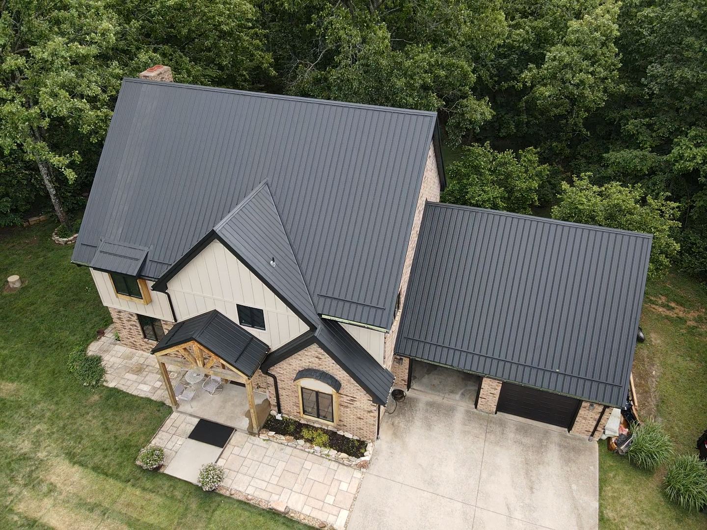 Aerial view of a white house with a gray roof and a wooden deck. Two white trucks are parked nearby.