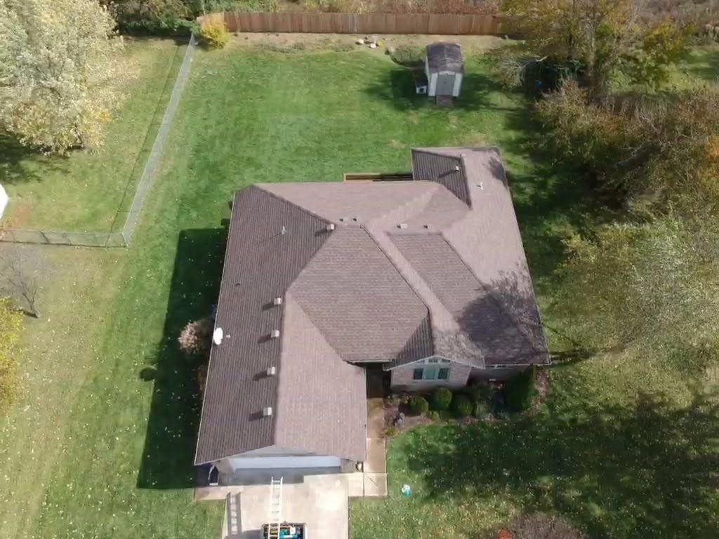 Overhead view of a house with a brown roof and a green lawn, shed in the back.